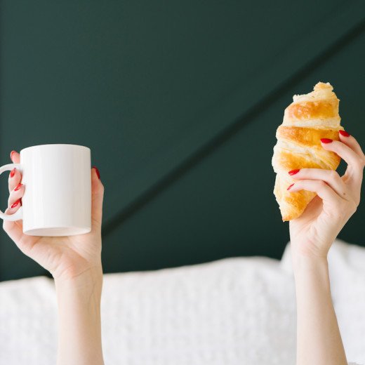 mains de femmes dans un lit tenant un mug blanc et un croissant